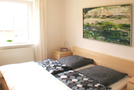 Schlafzimmer der Ferienwohnung in Laubegast mit Doppelbett, Kunstwerk und hellem Holzfußende