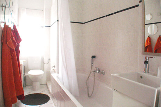 Badewanne mit Dusche und roten Handtüchern zum Aufhängen