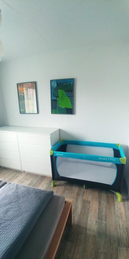 Wohnraum mit weißer Kommode, Bildern und blauem Babyreisebett